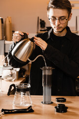 Barista is pouring hot water from drip kettle to aeropress. Process of brewing aeropress. Pouring hot water over roasted and ground coffee beans in aeropress.