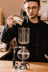 Barista pour ground coffee over syphon before starting boiling water inside siphon. Process of brewing syphon coffee in cafe.