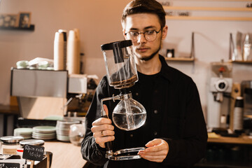 Barista is holding siphon before starting boiling water inside syphon. Process of brewing siphon coffee in cafe.