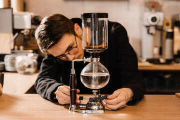 Barista is boil water in syphon device for alternative brewing coffee. Siphon vacuum pot for mixing coffee with boiling water.