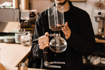 Barista is holding siphon before starting boiling water inside syphon. Process of brewing siphon coffee in cafe.