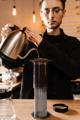 Barista is pouring hot water from drip kettle to aeropress. Process of brewing aeropress. Pouring hot water over roasted and ground coffee beans in aeropress.