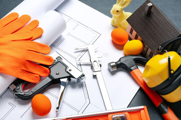 Construction tools with house model, plan and Easter eggs on dark background