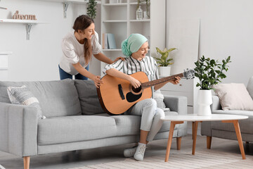 Teenage girl after chemotherapy playing guitar with her sister at home