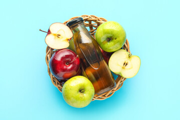 Basket with glass bottle of fresh apple cider vinegar and fruits on blue background