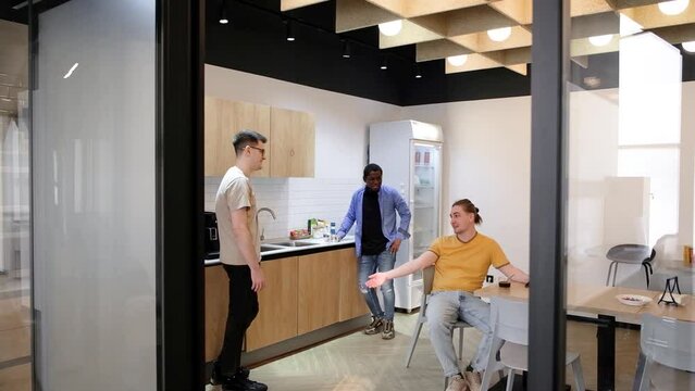 Group of cheerful young people talking and smiling during coffee break time in the office. Team of professional software developer relaxing in the canteen.
