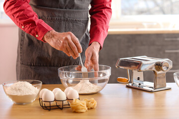 Man making dough for pasta at table in kitchen, closeup