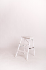 Wooden white ladder - stool. A room in a photo studio. White wall and floor. Copy space. Place for text and design.	