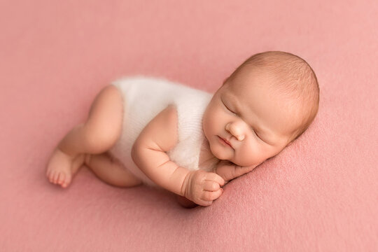 Top view of a newborn baby girl sleeping in a white overalls on a pink background. Beautiful portrait of a newborn baby 7 days, one week.