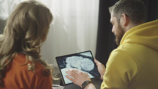 A man enlarges a picture of a child undergoing ultrasound diagnostics on a tablet. A pregnant woman and a man share a picture of the future child. High quality 4k footage