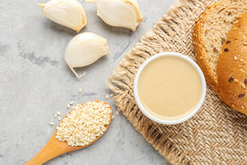 Bowl of tasty tahini, sesame seeds, garlic and bread on grunge background, closeup