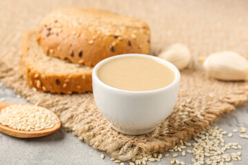 Bowl of tasty tahini, sesame seeds, garlic and bread on table, closeup
