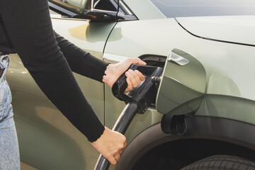 Hand of a young woman driving an EV or electric car holding DC power plug to her vehicle's green...