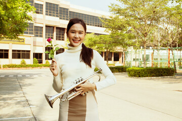 International music teacher in school : Portrait beautiful asian teacher healthy holding bright red rose and trumpet in front of school building handing flowers with friendly smile to lovely student. © ฺฺฺBoonterm