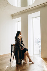 young beautiful girl sits on a chair and looks towards the window. girl posing on a chair in a photo studio with a minimalist design.