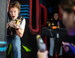 Portrait of positive young man with laser gun having fun with her friends on lasertag arena