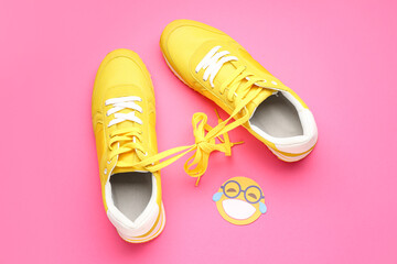 Sneakers with tied shoe laces and paper smile on pink background. April Fools' Day celebration