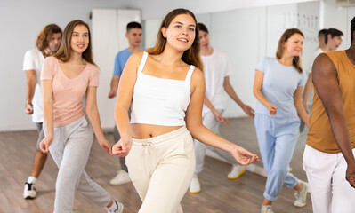 Group of sportive young adult diverse dancers performing dynamic movements during aerobic dance workout in gym