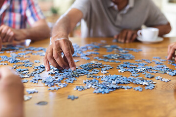 Hands of diverse senior friends sitting at table doing jigsaw puzzle together