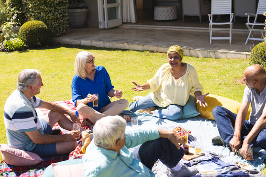 Happy group of diverse senior friends having picnic and talking in garden on sunny day