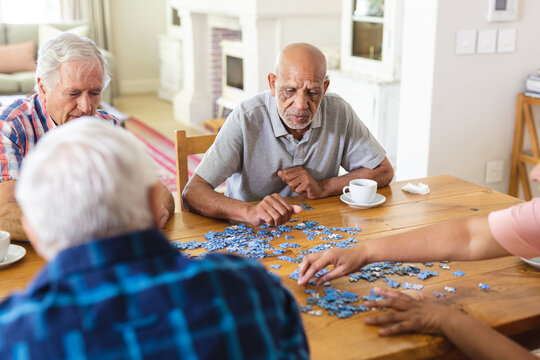 Focused group of diverse senior friends sitting at table doing jigsaw puzzle together