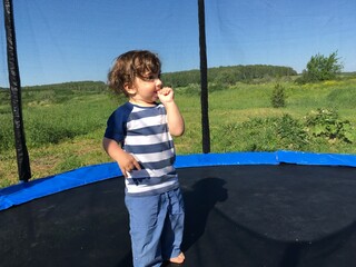 curly cute tender boy smiling child with a finger in his mouth stands on a trampoline
