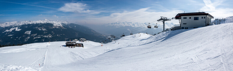 Fototapeta premium Upper station of the chairlift in a ski resort in the Austrian mountains. Cable car for skiers and a mountain panorama with a ski slope.