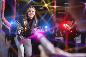 Joyous girl with laser pistol playing laser tag with friends on dark labyrinth