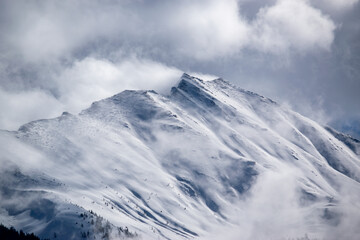 Fototapeta na wymiar Winter snowy ridge of rocky mountains in the Austrian Alps. Clouds around the top of the hill.