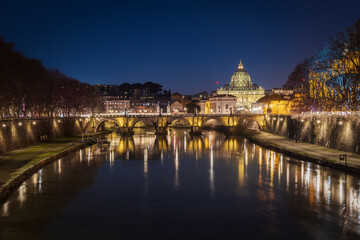 Cityscape with Sant Angelo bridge and St. Peter's cathedral at night with city lights in Rome, Italy
