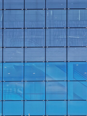 A fragment of an interesting modern building covered with glass against the background of the blue sky on a sunny day, Madrid, Spain.