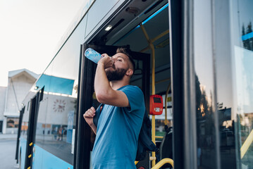 Man drinking bottle of water while getting off the bus