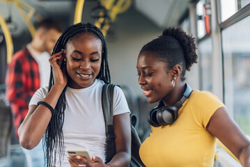 African american female friends using a smartphone while riding a bus in the city