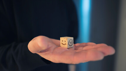 Satisfaction survey concept. Hand of a man holding a wood block cube with a smiley face on and confirming satisfaction.