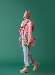 Stylish Muslim woman in pink hijab with bag on green background