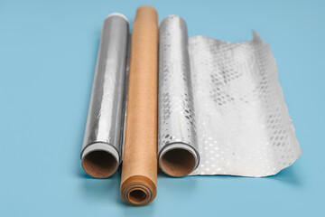 Rolls of aluminium foil and baking paper on color background