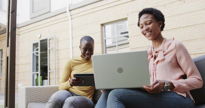 Two happy african american businesswomen talking, using technology outdoors, in slow motion