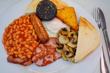 White board with full English breakfast with bacon, fried egg, beans, tomato, roasted sausage,...