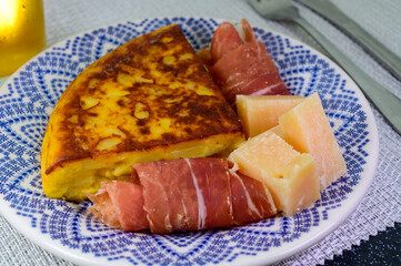 Spanish food, portion of potato omelette tortilla de patatas with onion served with cheese and jamon