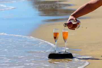 Pouring of rose champagne or cava sparkling wine served on white sandy tropical beach and blue ocean water, romantic vacation, winter sun on Fuerteventura, Canary, Spain
