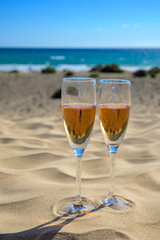 Two glasses of rose champagne or cava sparkling wine served on white sandy tropical beach with dunes and blue ocean, romantic vacation, winter sun on Fuerteventura, Canary, Spain