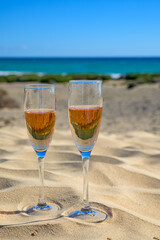 Two glasses of rose champagne or cava sparkling wine served on white sandy tropical beach with dunes and blue ocean, romantic vacation, winter sun on Fuerteventura, Canary, Spain