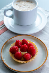 Breakfast with cup of black coffe and baked small tart with cream and fresh ripe red raspberry fruits