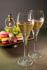 Glasses of sparkling white wine champagne or cava with bubbles and sweet dessert colorful macarons biscuits on background