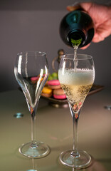Pouring of sparkling white wine champagne or cava with bubbles and sweet dessert colorful macarons biscuits on background