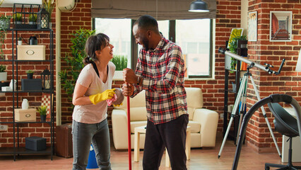 Life partners doing spring cleaning in apartment, mopping floors with all purpose cleaner and...