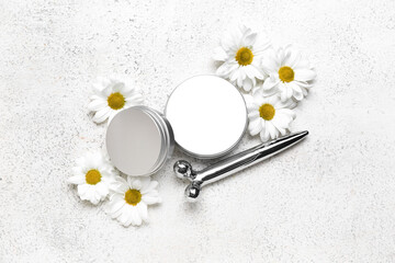 Obraz na płótnie Canvas Jars of cosmetic products, facial massage tool and chamomile flowers on light background