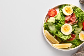 Plate of delicious salad with boiled eggs and jamon on grey background