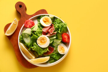 Board with plate of delicious salad on yellow background