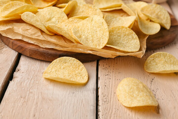 Board with delicious potato chips on white wooden background